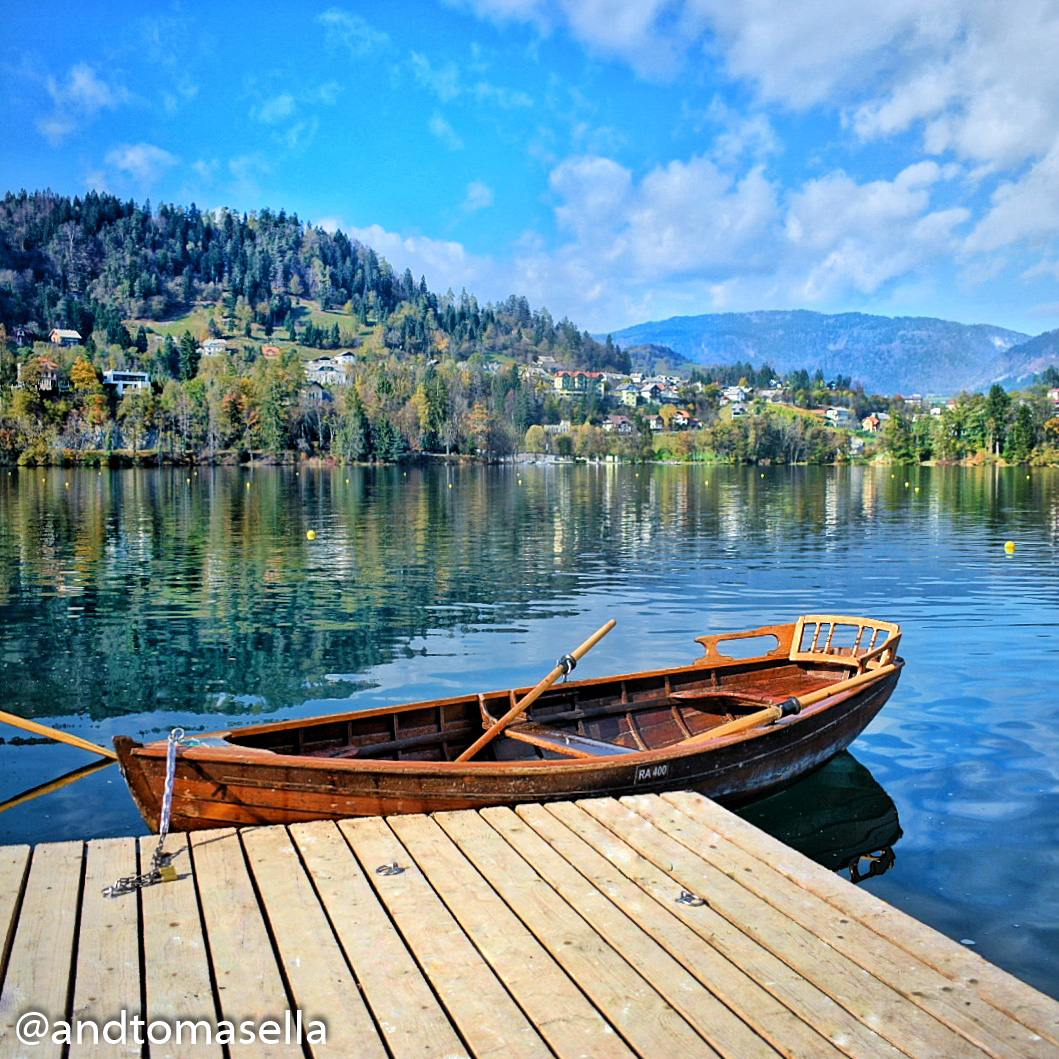 barca a remi ormeggiata sul lago di bled con collina e riflessi sul lago